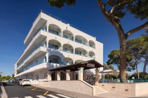un edificio bianco con auto parcheggiate davanti di Alcanada Golf Hotel a Port d'Alcudia
