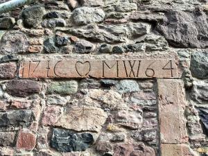 a sign on the side of a stone wall at Willesdene Cottage in Abernethy