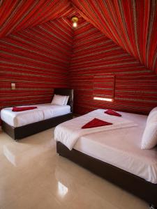 two beds in a room with a red wall at Starry Nights Camp in Wadi Rum