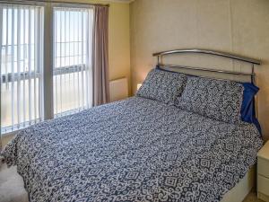 a bedroom with a bed with a blue comforter and two windows at Sandbank in Bacton