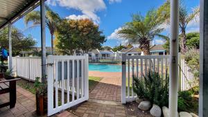 a white gate leading to a pool with trees and houses at Paradise Beach Cottage #20 in Jeffreys Bay