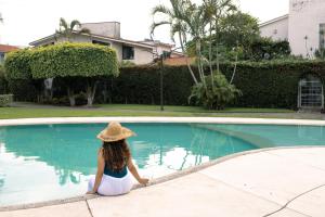 a woman in a hat sitting next to a swimming pool at Casa Viveros cerca de jardines 3 recamaras albercas y 2 estacionamientos in Jiutepec