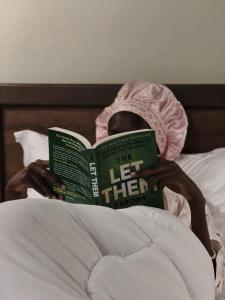 a woman laying in bed reading a book at Naigara hotel and suites in Kampala