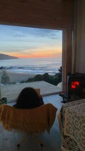 a person laying in a bed looking out a window at a view at Refugio en Tril tril in Bahía Mansa