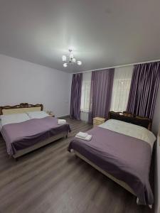 two beds in a bedroom with purple curtains and wooden floors at Narek B&B in Goris