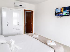 a white bedroom with a bed and a tv on the wall at Pousada Escarpas in Capitólio