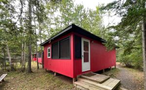 a red cabin with a black roof in the woods at Forest & Lake PEI Cottages in Murray Harbour