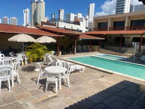 a patio with white chairs and tables and a pool at Ponta Negra Palace in Natal