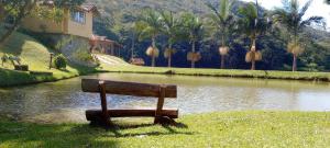 a bench sitting in the grass next to a river at Hotel Fazenda Upã Moña in Vassouras