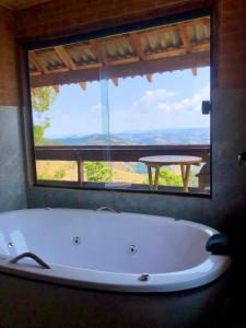 a bath tub in a bathroom with a large window at Chalé Theo - Para momentos únicos in Camanducaia