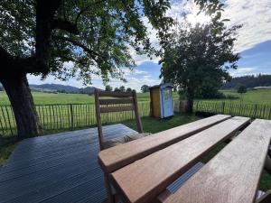 a wooden bench sitting on a deck next to a tree at Genau So - Schäferwagen in Maierhöfen