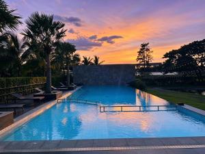 a large swimming pool with a sunset in the background at iChapter Hotel Suvarnabhumi in Samutprakarn