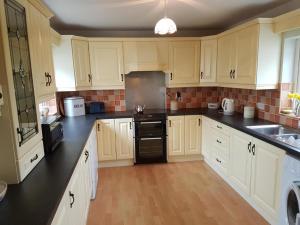 a large kitchen with white cabinets and black appliances at Culoort Cottage - Malin Head in Malin Head