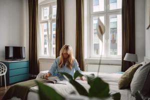 a woman sitting on a bed reading a book at Apartamenty Młyńska15 self check-in 24h in Katowice