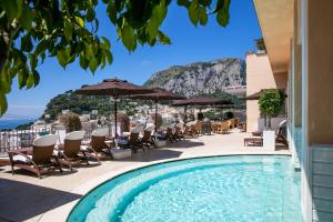 a pool on the roof of a hotel with chairs and umbrellas at Capri Tiberio Palace - The Leading Hotels of the World in Capri