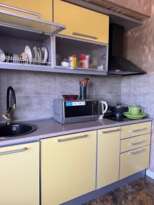 a kitchen with yellow cabinets and a microwave at Абдрахманова 176 in Bishkek