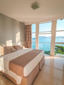a bedroom with a large bed with large windows at Grand Hotel Guarujá - A sua Melhor Experiência Beira Mar na Praia! in Guarujá
