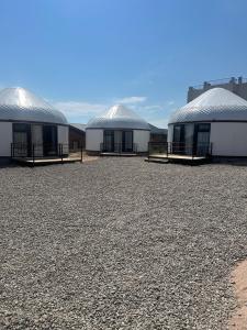 three buildings with domes on top of a gravel field at Tangnuru eco yurts in Bosteri