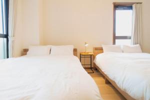 two beds with white sheets in a room with a window at Haul Sakuramachi in Kumamoto