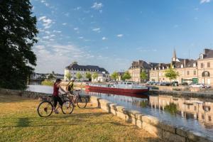 two people riding bikes next to a river with a boat at Ar gwelva in Cléguérec