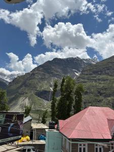 a building with a red roof with mountains in the background at Radhakrishna Homestay in Kulu