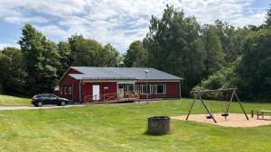 a red shed with a playground and a car parked in front at Örkelljunga Hostel in Orkelljunga