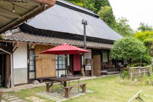 a picnic table with a red umbrella in front of a building at ゲストハウス やまんなか in Kamida