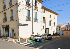 two cars parked in a parking lot in front of a building at Appartement tout confort avec balnéo et lit king size in Pézenas