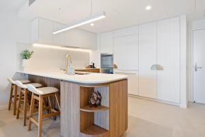 a kitchen with white cabinets and a counter with stools at Luxury Esprit Apartment at Rainbow Bay in Gold Coast