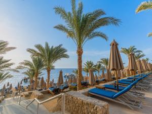 a row of beach chairs with umbrellas and palm trees at Xperience Sea Breeze Resort in Sharm El Sheikh