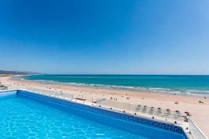a swimming pool next to a beach with people at Apartamentos Playa Barbate in Barbate