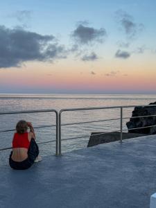 a woman sitting on a pier looking at the ocean at Casa do Porto - Santa Cruz B&B in Ribeiras