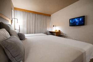 ein Hotelzimmer mit einem großen weißen Bett und einem Flachbildfernseher in der Unterkunft Intercity Campinas in Campinas