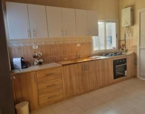a large kitchen with wooden cabinets and a window at home byrsa in Douar ech Chott
