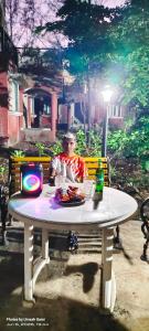 a man sitting at a white table in a park at Marigold Bungalow in Kelavli