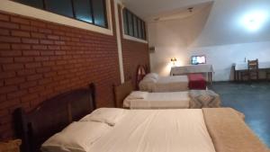 a room with three beds and a table with a television at Pousada Vila Bela in Poços de Caldas
