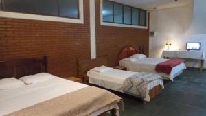 a room with three beds and a brick wall at Pousada Vila Bela in Poços de Caldas