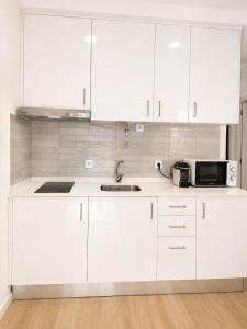a white kitchen with white cabinets and a microwave at Casa Candil in Nazaré