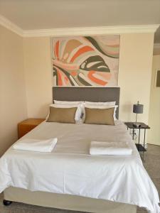 a white bed with two pillows and a painting on the wall at Kairos Guest House in Maseru