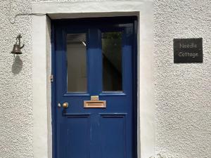 a blue door in a white building with a bell at Needle Cottage in Cullen