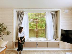a woman sitting in front of a window at Private Rock Onsen Villa Orin & Zen Garden in Shiraoi