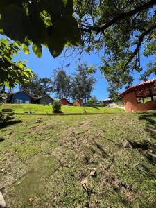 a field of grass with a house in the background at Chale Vermelho Aconchegante com lareira no bosque e estacionamento grátis in Extrema