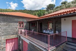 a stone house with red doors and a balcony at Feel Discovery Casa Fonte do Lagar in Desejosa