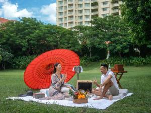 a man and woman sitting on a picnic blanket with an umbrella at Sofitel Phnom Penh Phokeethra in Phnom Penh