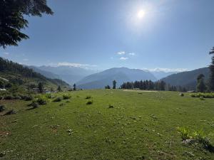 a field of green grass with mountains in the background at Magic Valley Devroopa Trek - Pickup and drop to New Delhi in Kulu
