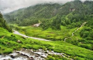 a green hillside with a river and a road at Magic Valley Devroopa Trek - Pickup and drop to New Delhi in Kulu