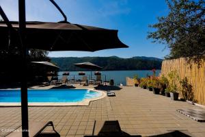 a swimming pool with an umbrella next to a lake at Pensiunea Celestin in Eşelniţa