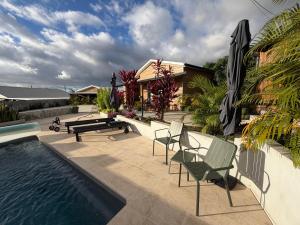 a patio with a pool and chairs and an umbrella at O coeur de l'ouest Bungalow Maloya in Le Bois de Nèfles