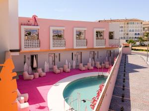 a resort with a swimming pool and chairs and a building at On Pink Motel in Matalascañas
