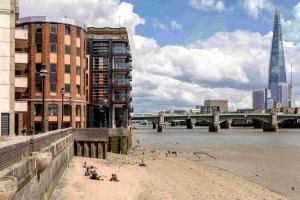 a beach next to a river with buildings and a bridge at Locke at Broken Wharf in London